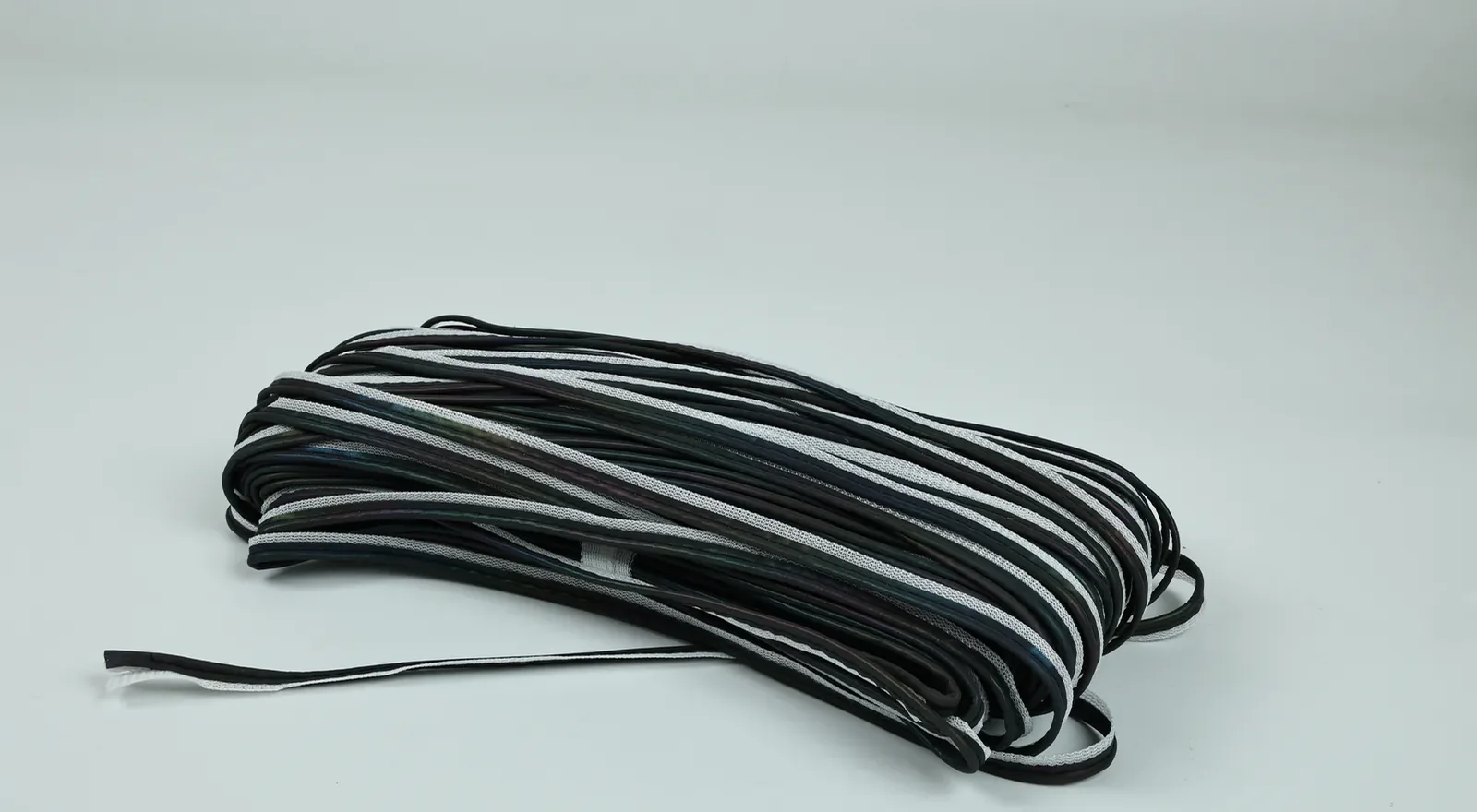 Folded bundle of black MP0103 piping with narrow silver-gray edges on a light background